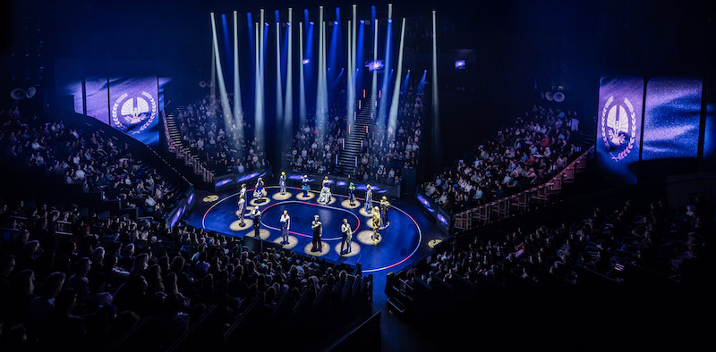 Aerial shot of the whole theatre, with characters circled around the stage looking in the direction of the audience